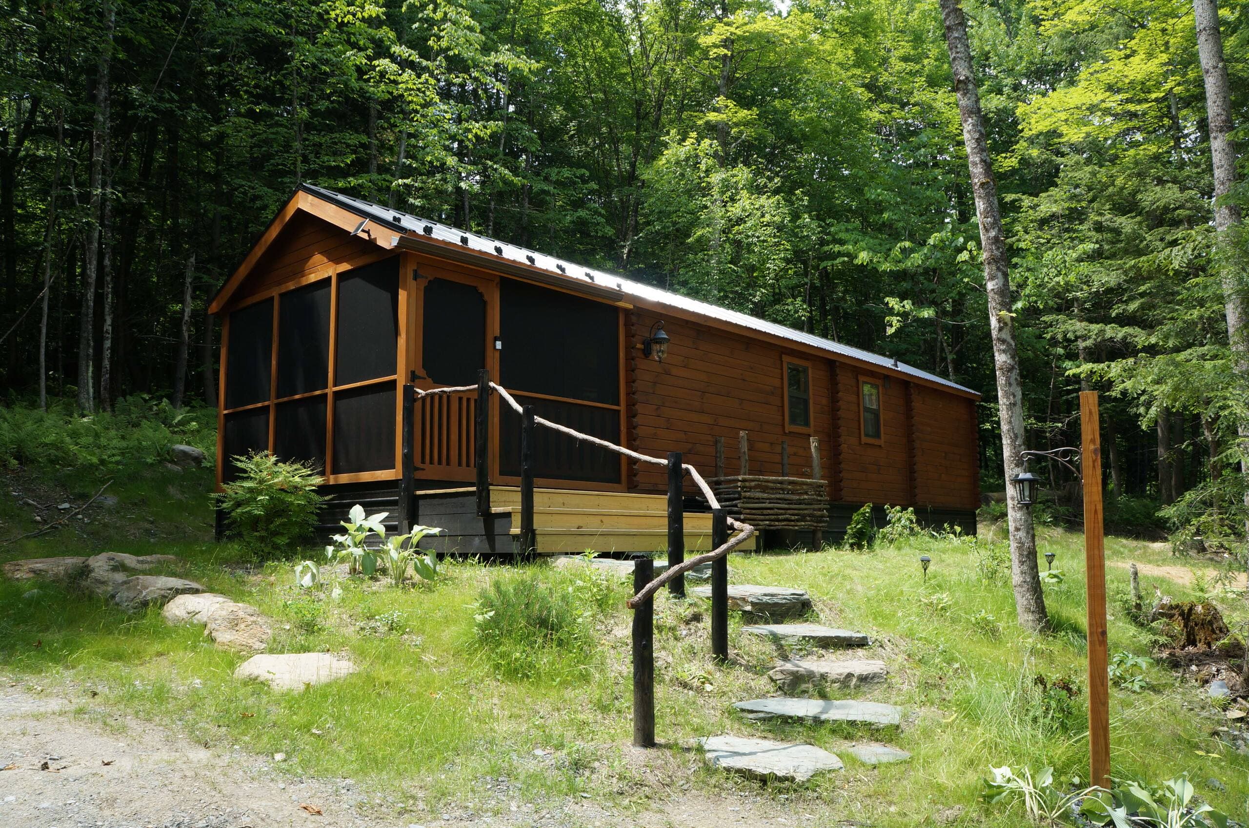 Alchemist’s Log Cabin exterior with screened porch, tucked into the summer forest