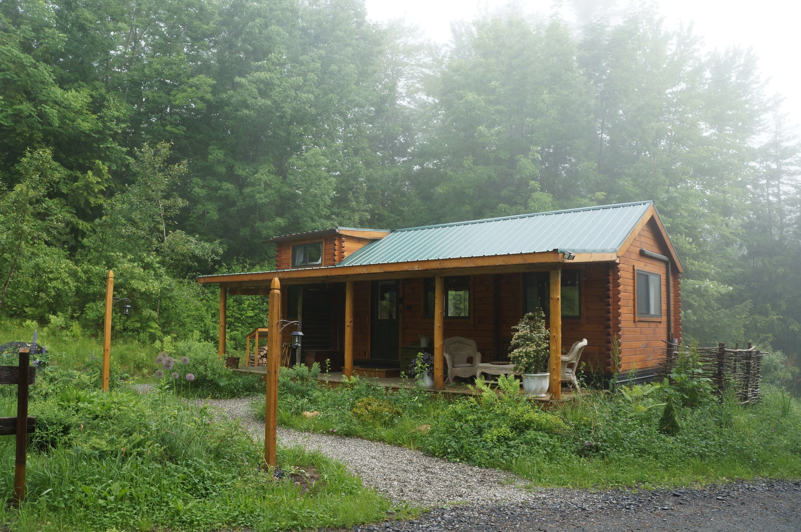 A Moonlight Woods log cabin glowing in the misty Vermont morning, a garden path leading to the porch
