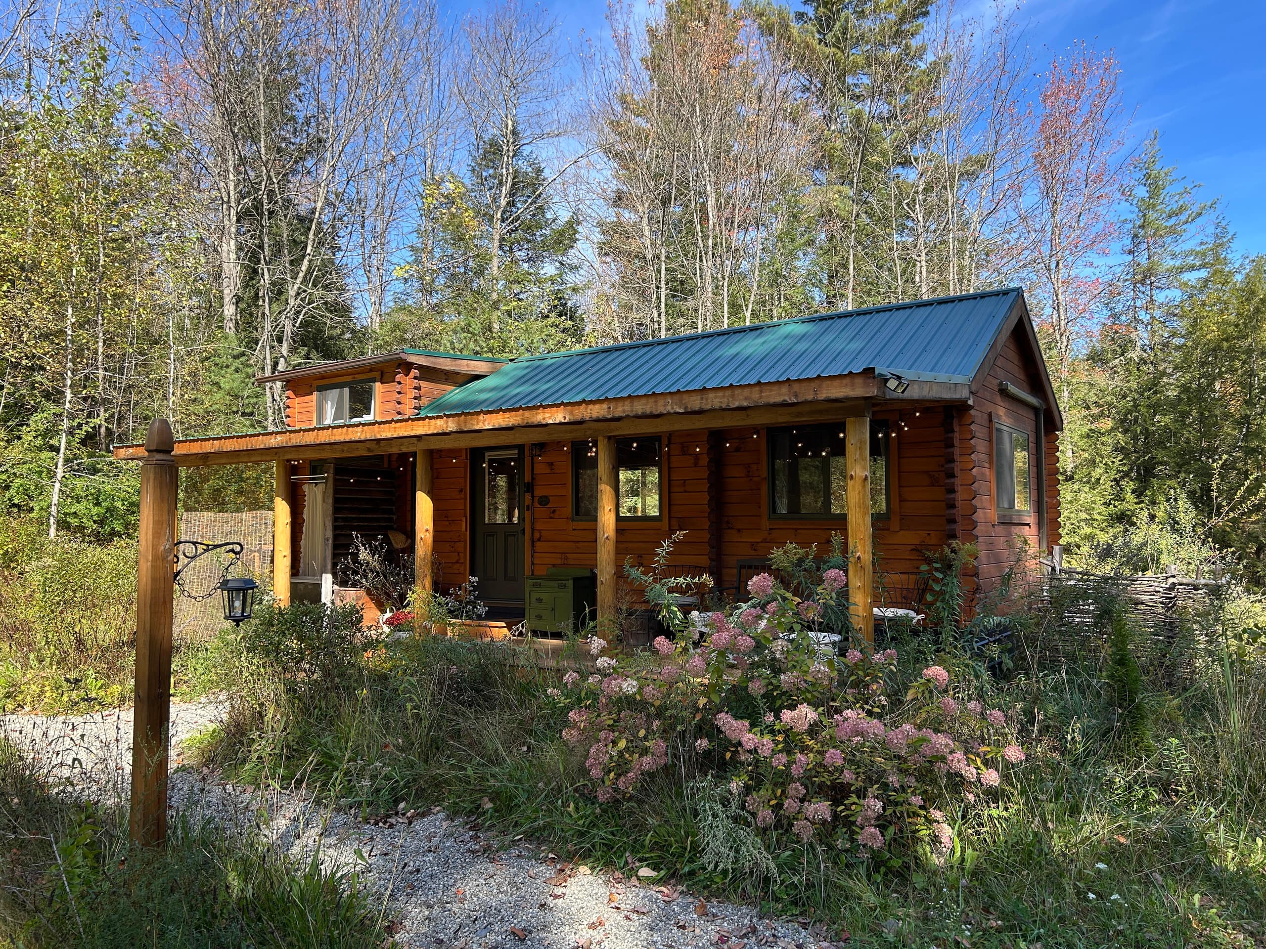 Gardener’s Log Cabin exterior with covered porch and cottage garden at the forest edge